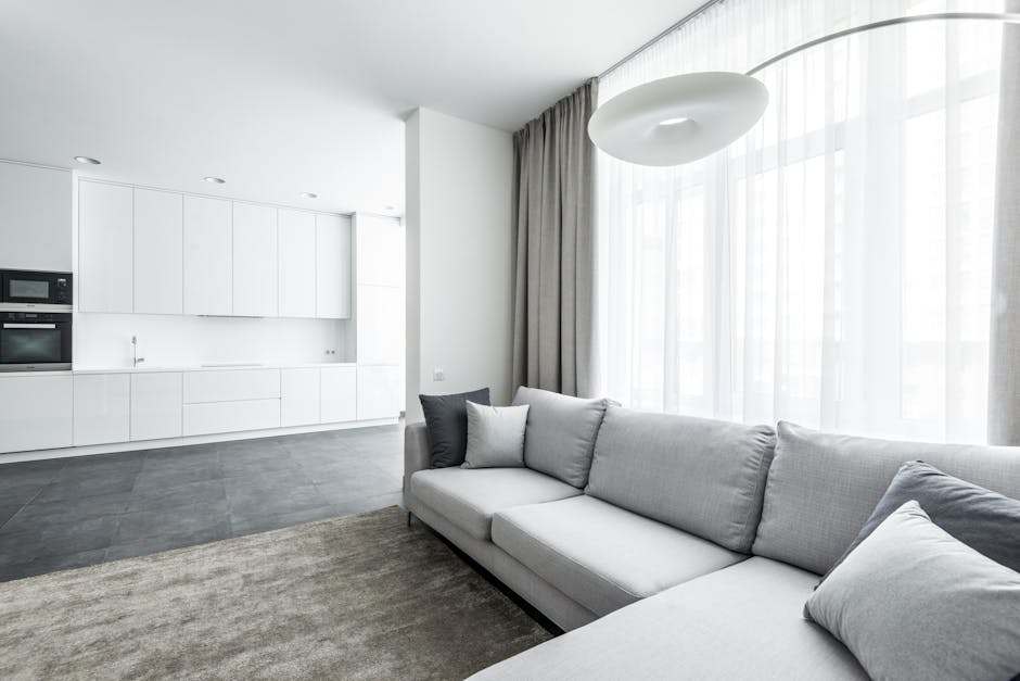 A white tufted fabric sofa with rolled arms and dark wooden legs is positioned against a white paneled wall inside a room with wooden flooring. The sofa appears clean and well-maintained, with no visi
